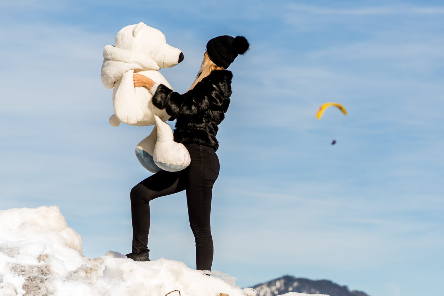 A cheerful girl hugging a teddy bear in the snow, in front of SissiPark.